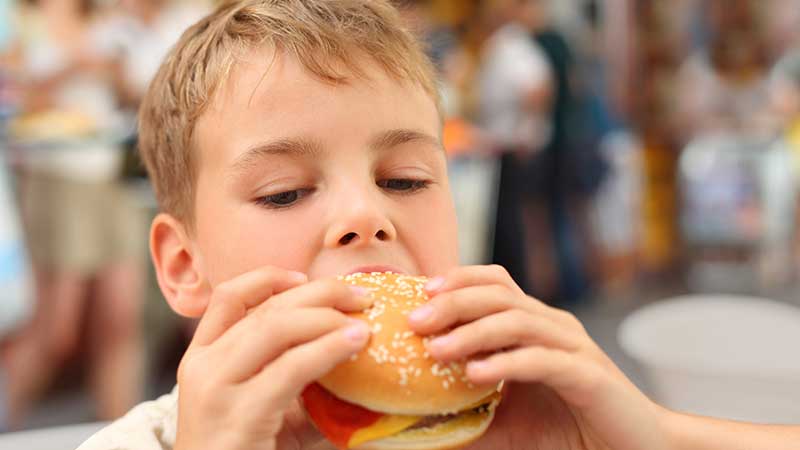 criança a comer um hambúrguer com queijo e ketchup na escola